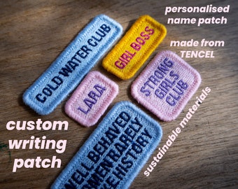 Op de afbeelding: Vijf geborduurde patches op een houten oppervlak. De patches zijn in verschillende kleuren en bevatten verschillende zinnen, waaronder "Cold Water Club", "Girl Boss", "Strong Girls Club", "Well Behaved Men Rarely Make History" en "Lara". De tekst "gepersonaliseerde naam patch gemaakt van TENCEL duurzame materialen custom writing patch" staat op het oppervlak.