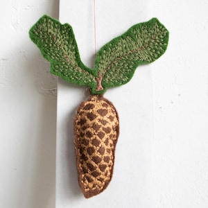 May include: Embroidered pinecone ornament with green leaves and a brown stem. The pinecone is brown with a tan diamond pattern. The leaves are green with brown veins. The ornament is hanging from a thin string.