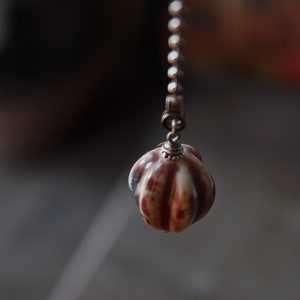 May include: A brown and white ceramic light pull with a silver chain.
