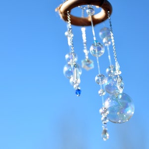 Puede incluir: Un anillo de madera con un carill&oacute;n de cuentas colgando de &eacute;l. El carill&oacute;n est&aacute; hecho de cuentas de vidrio transparente y cuentas azules. El carill&oacute;n est&aacute; colgando contra un cielo azul.