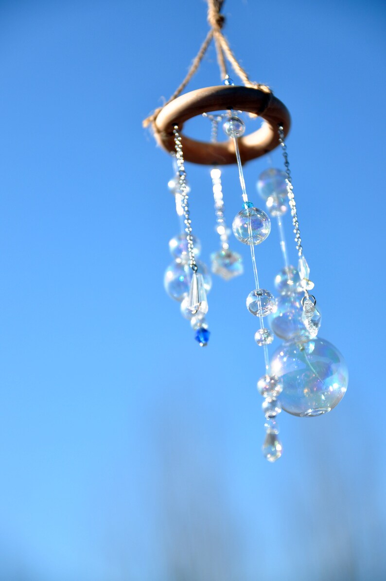 Puede incluir: Un anillo de madera con un carill&oacute;n de cuentas colgando de &eacute;l. El carill&oacute;n est&aacute; hecho de cuentas de vidrio transparente y cuentas azules. El carill&oacute;n est&aacute; colgando contra un cielo azul.