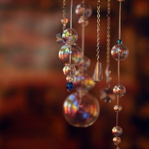 Puede incluir: Un carill&oacute;n de viento de vidrio con cuentas de vidrio iridiscentes y detalles de cristal azul que cuelgan de un anillo de madera.