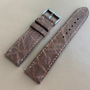 Może przedstawiać: Brązowy skórzany pasek do zegarka z białymi szwami. Pasek ma fakturowaną powierzchnię przypominającą skórę słonia.
