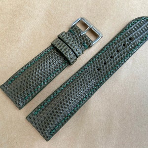Könnte beinhalten: Ein dunkelgrünes Lederarmband mit strukturierter Oberfläche und grünen Nähten. Das Armband hat eine silberne Schließe.