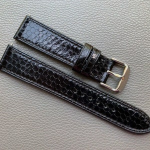 May include: A black leather watch strap with a textured, snake-like pattern. The strap has a silver buckle.