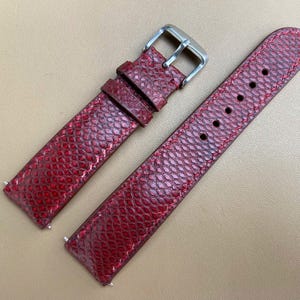 May include: A red leather watch strap with a silver buckle. The strap has a textured surface that resembles scales.
