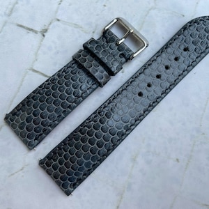 May include: A gray leather watch strap with a textured pattern. The strap has a silver buckle.
