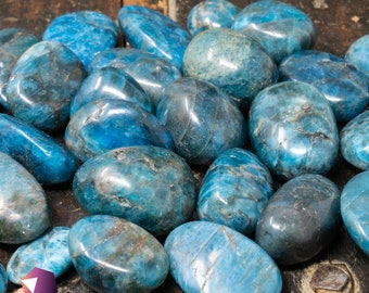 Puede incluir: Una colección de piedras de apatita azul lisas y pulidas. Las piedras son de varios tamaños y formas, con un color azul claro y un ligero brillo iridiscente.