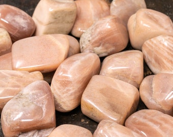 May include: A collection of tumbled sunstone stones in various shades of peach and orange. The stones are smooth and polished, with a subtle shimmer.