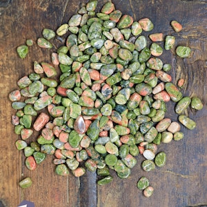 May include: A pile of green, red, and white tumbled stones. The stones are smooth and polished, and they are arranged in a random pattern. The stones are on a wooden surface.