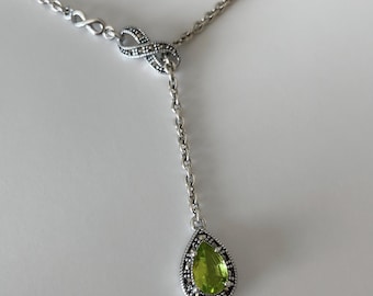 May include: A silver necklace with an infinity symbol and a pear-shaped green gemstone pendant.
