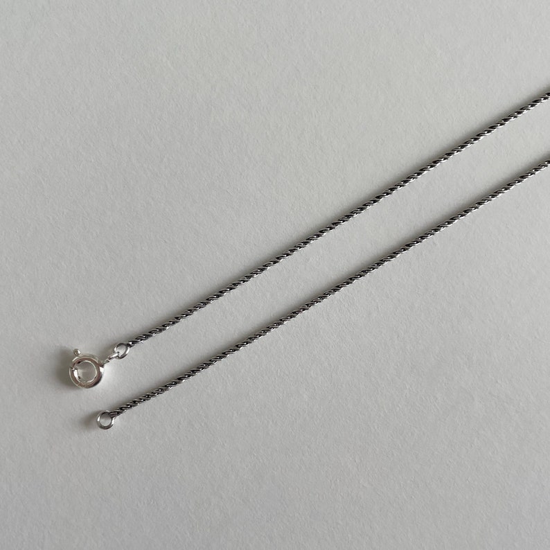 May include: A silver chain necklace with a twisted design. The chain is approximately 18 inches long and has a lobster clasp closure.