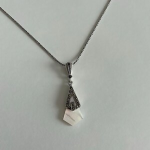 May include: A silver chain necklace with a pendant featuring a white shell with a silver and black marcasite design.