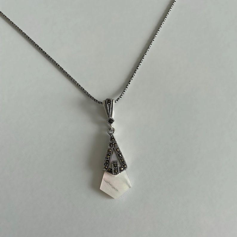 May include: A silver chain necklace with a pendant featuring a white shell with a silver and black marcasite design.