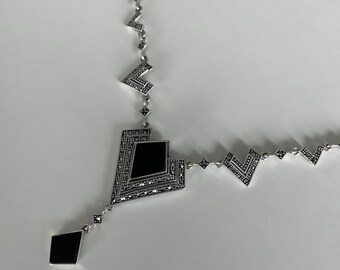 May include: A silver necklace with a black onyx pendant. The pendant is shaped like a diamond and has a geometric design. The necklace is made of silver and has a delicate chain.