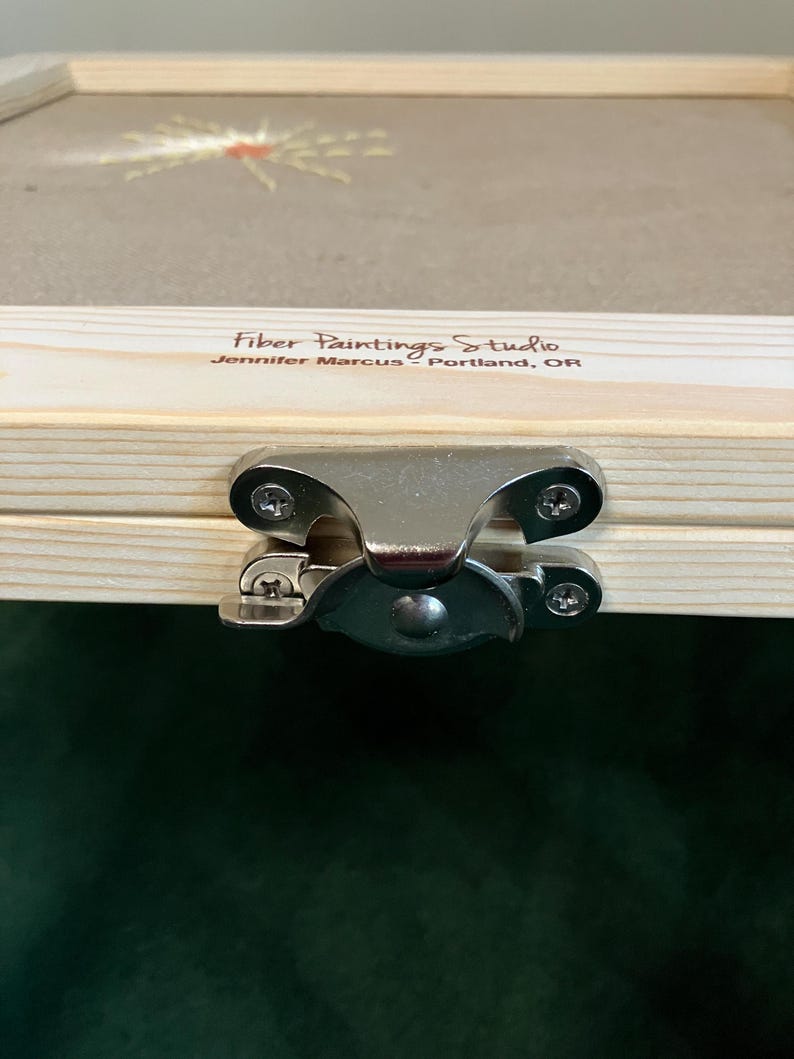 May include: Close-up of a wooden box with a metal clasp. The box has a clear top with a fiber art design. The text "Fiber Paintings Studio" and "Jennifer Marcus - Portland, OR" is printed on the wood.