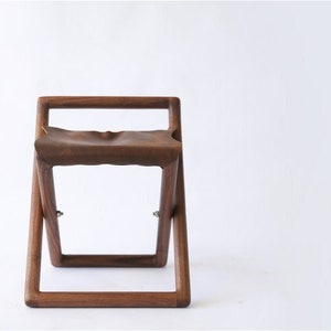 May include: A dark brown wooden folding stool with a leather seat.