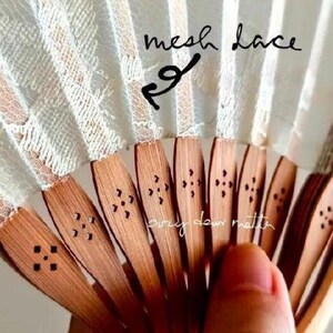 May include: A folding hand fan featuring light-colored mesh lace fabric attached to wooden ribs. The wooden ribs have a natural brown finish and are decorated with small, laser-cut floral patterns. The text mesh lace is written on the fan.