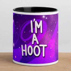 May include: A white ceramic mug with a black rim. The mug has a purple galaxy background with white text that reads "I'm a HOOT".