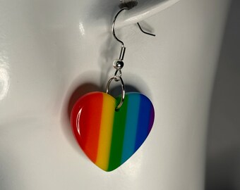 Könnte beinhalten: Regenbogenförmige Herz-Ohrringe mit einem silbernen Haken. Das Herz ist aus farbigem Harz und zeigt die Farben des Regenbogens.
