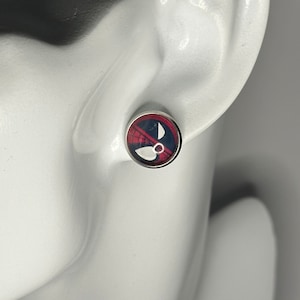May include: A pair of silver stud earrings featuring a red, black and white image of a superhero's face.
