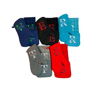 May include: Set of ten oven mitts in various colors, including red, blue, gray, and black. Each mitt features a quilted design and a personalized name embroidered in a contrasting color. The names include Ventura, Trinidad, Escobal, Roa, and So.