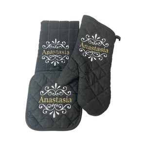 May include: Black quilted oven mitts and a matching pot holder with the name Anastasia embroidered in gold and white on each piece.