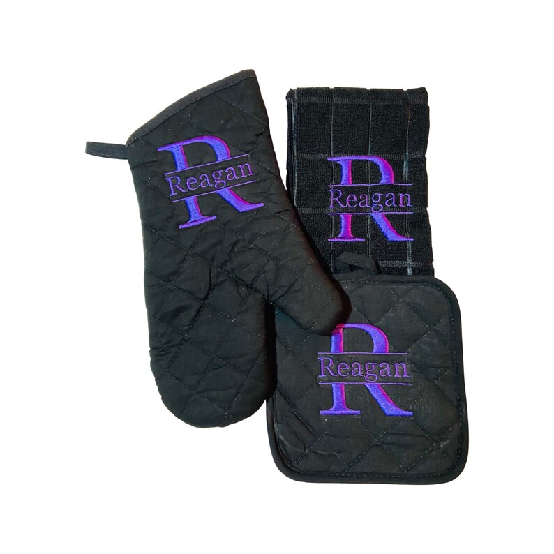 May include: Black quilted oven mitt, pot holder, and kitchen towel set with the name "Reagan" embroidered in purple on each piece.