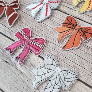 Peut inclure: Un ensemble de dix patchs brodés thermocollants représentant des nœuds sur le thème du sport. Les nœuds sont de différentes couleurs, notamment rose, blanc, orange, jaune et marron. Chaque nœud a un design différent sur le thème du sport, comme le baseball, le football américain, le basketball et le football.