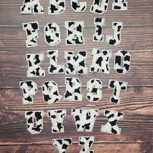 Peut inclure: Un ensemble de 26 lettres majuscules en motif vache. Les lettres sont blanches avec des taches noires et ont un contour argent&eacute; paillet&eacute;. Les lettres sont dispos&eacute;es en ordre alphab&eacute;tique.