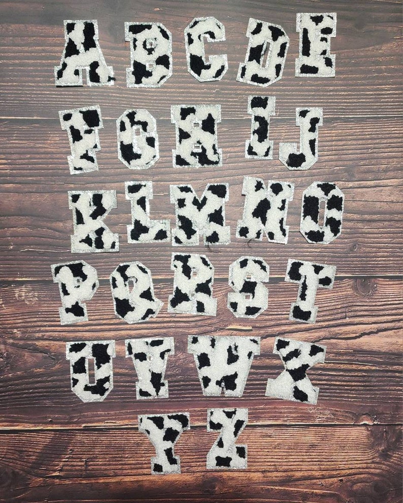 Peut inclure: Un ensemble de 26 lettres majuscules en motif vache. Les lettres sont blanches avec des taches noires et ont un contour argent&eacute; paillet&eacute;. Les lettres sont dispos&eacute;es en ordre alphab&eacute;tique.