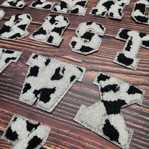 Peut inclure: Un ensemble de lettres thermocollantes &agrave; imprim&eacute; vache noir et blanc. Les lettres sont en gras, en caract&egrave;res gras et sont parfaites pour ajouter une touche de personnalit&eacute; aux v&ecirc;tements, aux sacs ou &agrave; d'autres articles en tissu.