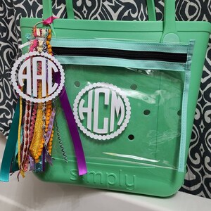 May include: A green clear tote bag with a zippered pocket and a white monogram that says "HCM". The bag has the word "simply" embossed on the bottom. A white monogram keychain with the letters "AAC" is attached to the bag.