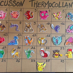 Op de afbeelding: Een kartonnen displaybord met het opschrift ECUSSON THERMOCOLLANT met dertig genummerde rastervakken, elk met een unieke geborduurde strijkpatch die verschillende kleurrijke stripfiguren in diverse houdingen en levendige kleurenschema's toont.
