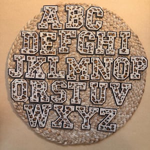 Peut inclure: Un alphabet complet de patchs thermocollants, chaque lettre dans un style gras et en bloc. Les lettres présentent un motif léopard avec une bordure blanche et sont disposées sur un dessous de plat rond et tissé. Les lettres sont en majuscules.