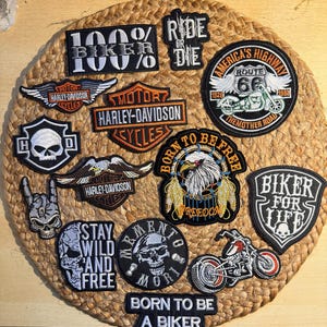 Può includere: Una collezione di toppe da motociclista ricamate in varie forme e dimensioni. Le toppe includono frasi come "100% Biker", "Ride or Die" e "Born to be Free". Sono presenti anche loghi Harley-Davidson e immagini della Route 66.