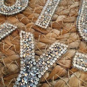 May include: A collection of alphabet letter patches covered in clear, faceted rhinestones. Each letter features a dense arrangement of sparkling, multi-faceted crystals set against a transparent backing, creating a reflective and textured surface.