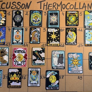 May include: A collection of rectangular embroidered iron-on patches arranged on a grid board labelled ECUSSON THERMOCOLLANT. The patches feature various mystical and celestial designs, including tarot-style imagery of suns, moons, stars, and figures, with vibrant thread colours on black or coloured backgrounds.