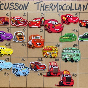 Peut inclure: Une collection d'écussons thermocollants brodés représentant divers personnages de voitures de dessin animé du film Cars, disposés sur une grille numérotée de 1 à 30. Les écussons incluent des voitures de course rouges, des camions et des vans.