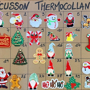 Peut inclure: Une collection d'écussons thermocollants brodés sur le thème de Noël, disposés sur une grille intitulée ECUSSON THERMOCOLLANT. Les motifs incluent le Père Noël, des gnomes, des bonhommes de neige, des rennes, des pains d'épices et des sapins.