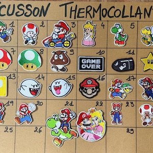 Peut inclure: Une collection de trente écussons thermocollants brodés représentant divers personnages et icônes de Super Mario, dont Mario, Luigi, Princesse Peach, Yoshi, Toad et un panneau Game Over, disposés sur une grille numérotée de 1 à 30.