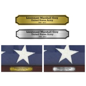 May include: Two framed American flags with gold and silver plaques below. The plaques read "Lieutenant Marshall Grey United States Army 1965-2017".