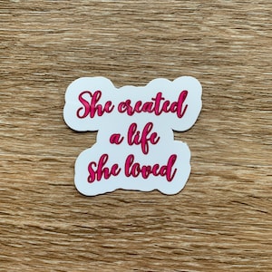 Può includere: Etichetta bianca con testo rosa che dice "She created a life she loved".