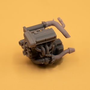 Puede incluir: Un modelo de motor de coche de plástico gris detallado con tubos de escape.