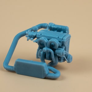 Könnte beinhalten: Ein blaues 3D-gedrucktes Modell eines Automotors mit detailliertem Design. Der Motor ist auf einem Ständer montiert, mit einem Rohr, das ihn mit dem Motor verbindet.