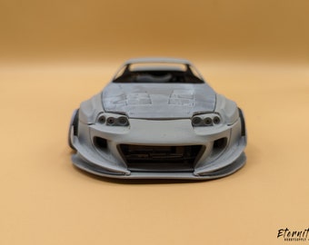 May include: A gray model car with a wide body kit, visible headlights, and a detailed front bumper. The car is set against a tan background, showcasing its design. The text "Eternity Hobbysupply" is in the bottom right corner.