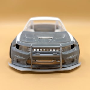 Op de afbeelding: Een grijze en witte model auto met een zwarte grille en een voorbumper met een metalen kooi. De auto is een Dodge Charger.