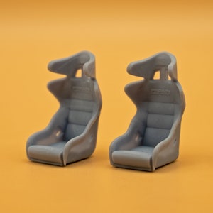 Puede incluir: Dos asientos de carreras grises con reposacabezas. Los asientos tienen una superficie texturizada y la palabra "PROADV" está impresa en la parte posterior de cada asiento.