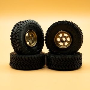 May include: Four black tires with gold rims stacked on top of each other. The tires have a tread pattern and the rims have a six-spoke design.