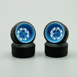 Puede incluir: Cuatro neumáticos de coche en miniatura negros y azules con un patrón de banda de rodadura detallado. Los neumáticos están apilados en pares, con las llantas azules hacia afuera.